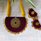 Maroon and gold necklace with matching earrings on a light fabric background